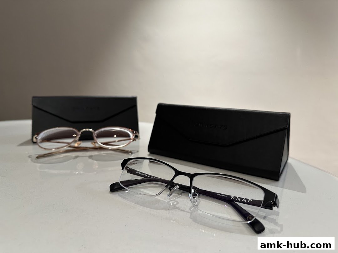 Two pairs of eyeglasses with their cases are displayed on a white surface.