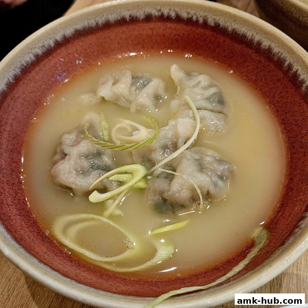 A close-up shot of delicious dumplings in a savory broth, garnished with fresh scallions.