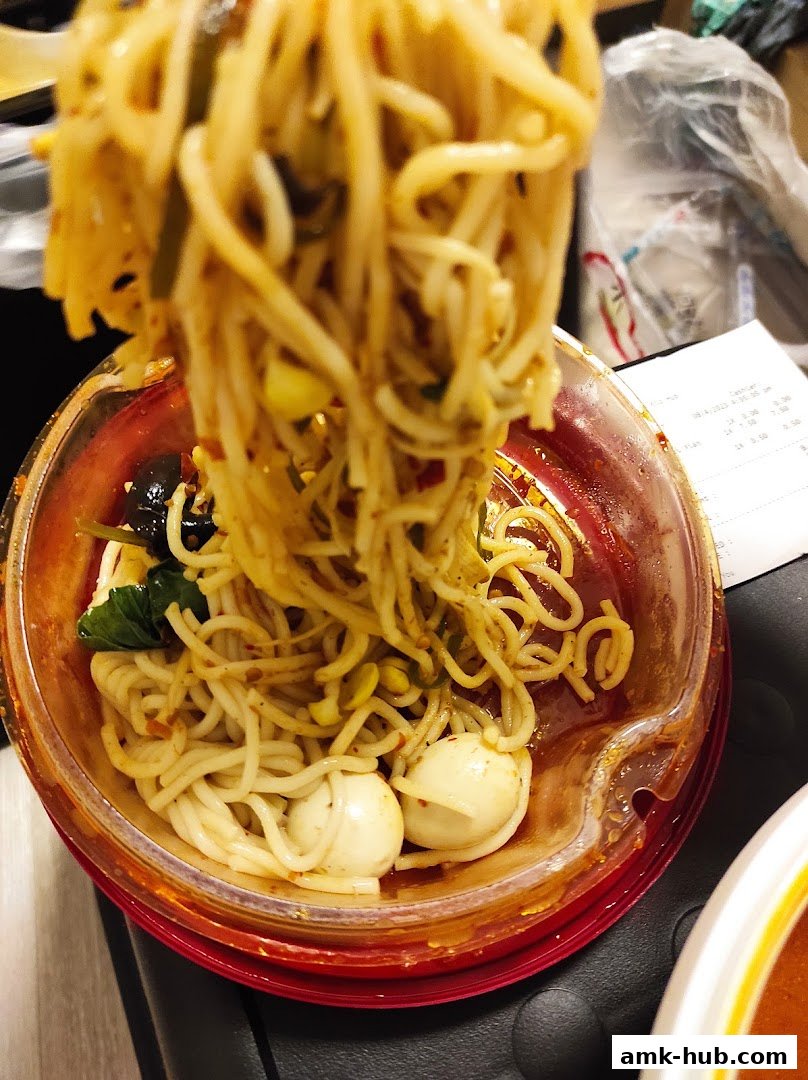 A close-up shot of a bowl of noodles with various ingredients and a receipt in the background.