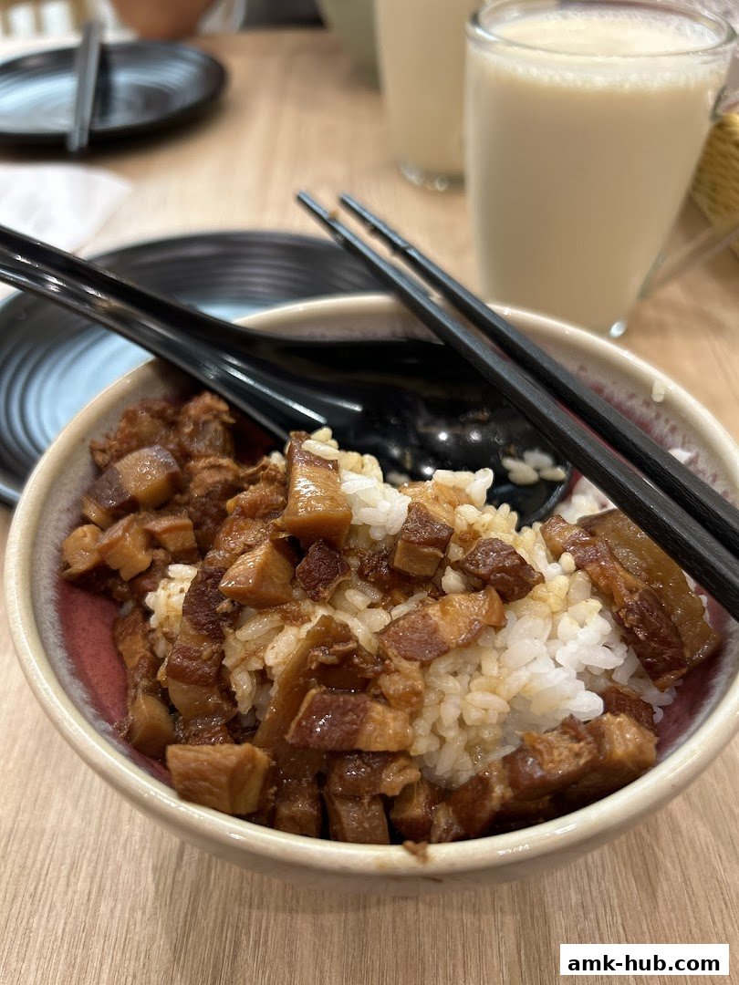 A close-up of a bowl of braised pork rice with chopsticks and a drink.