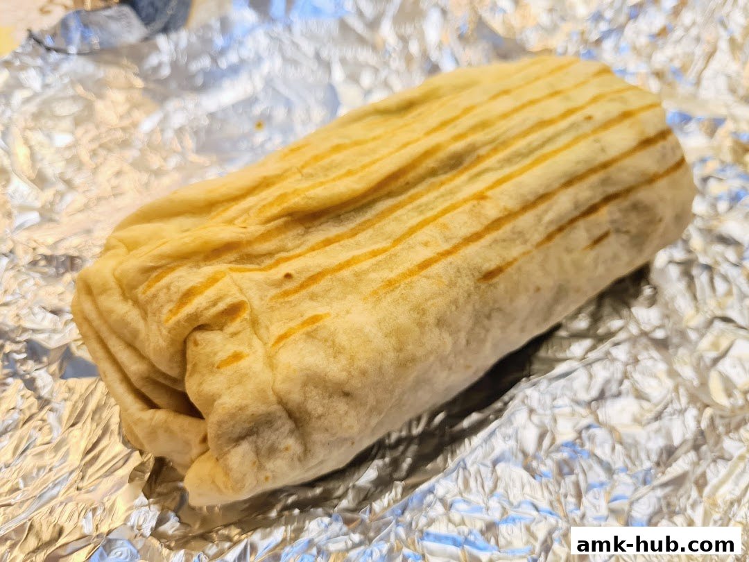A close-up shot of a grilled burrito wrapped in foil.