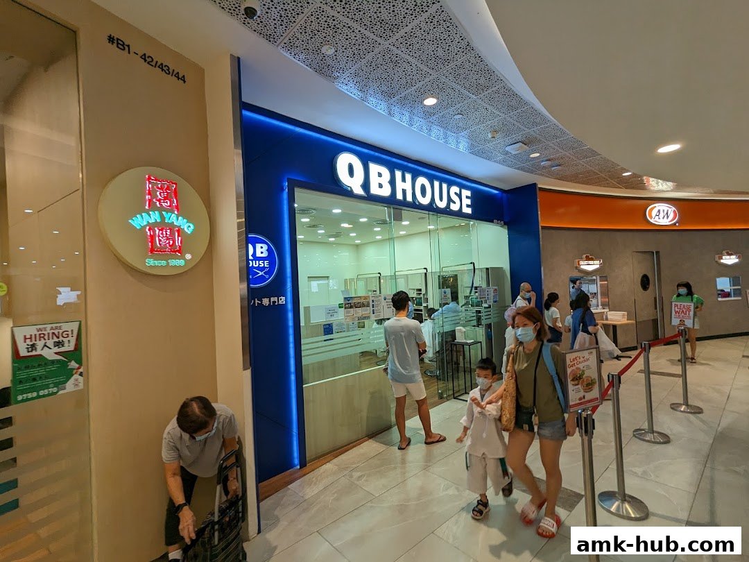 The QB HOUSE shop entrance with customers waiting in line and a neighboring restaurant.
