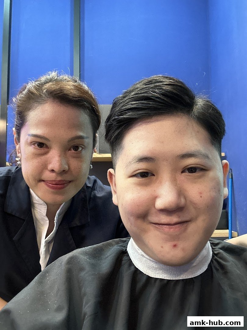 Two people, likely a barber and a client, smiling for a selfie in a barber shop.