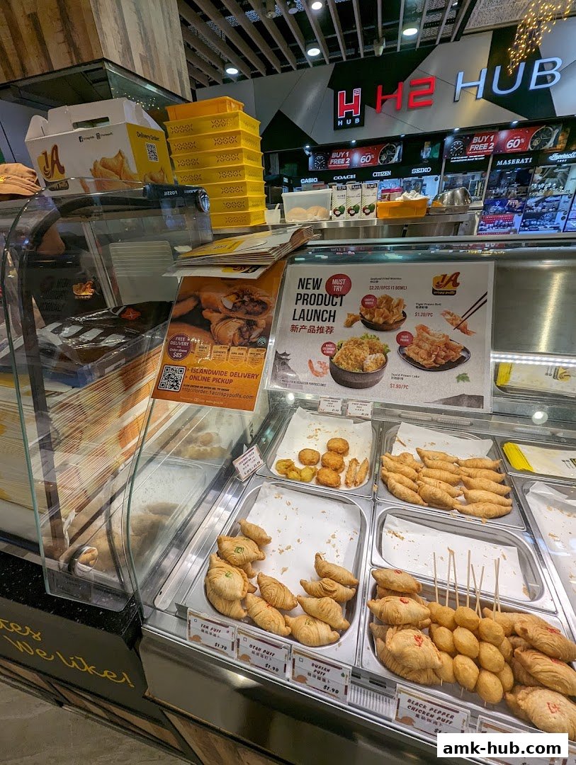 A display case filled with various fried snacks and pastries, with promotional posters in the background.