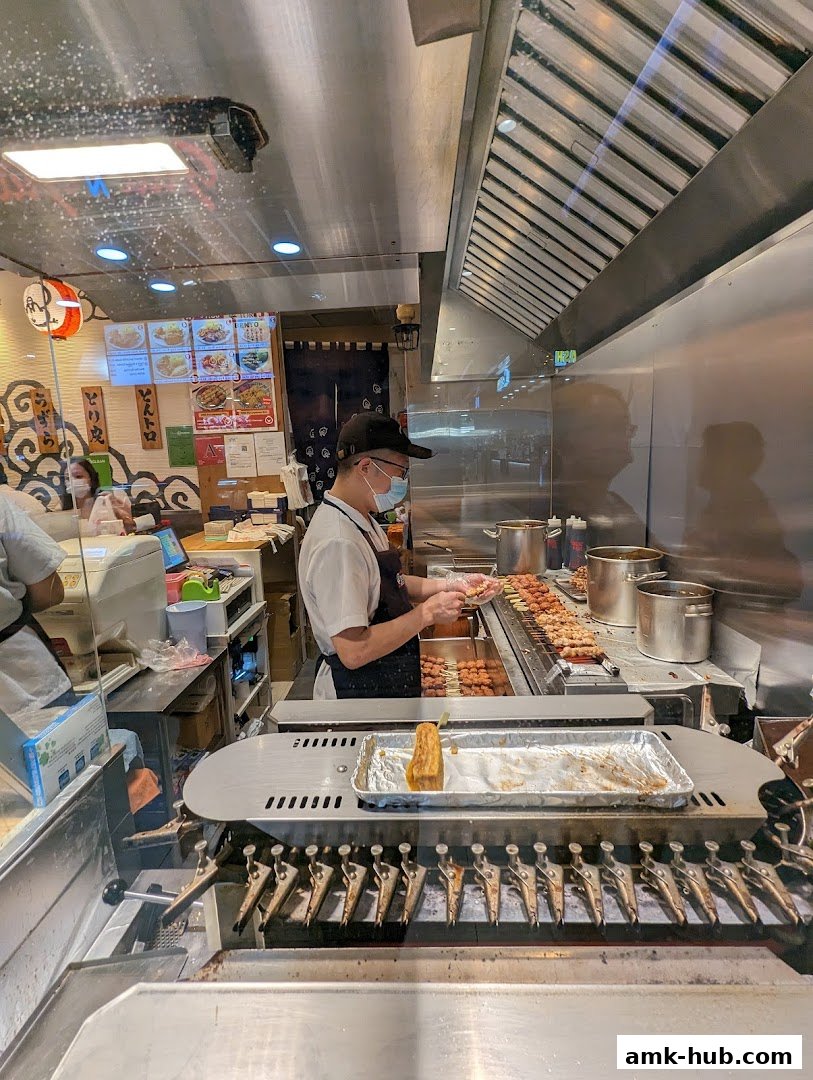 A chef prepares skewers of food behind a counter at a Japanese restaurant.