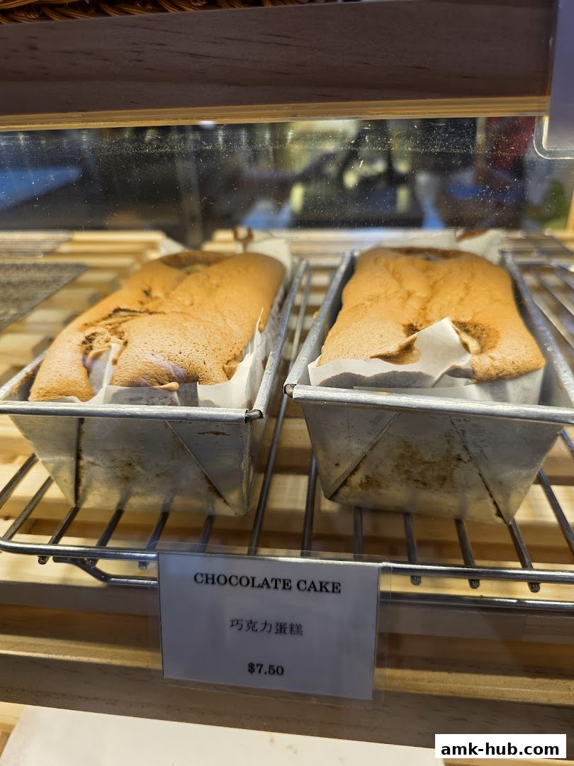 Two loaves of chocolate cake displayed in metal pans on a wire rack.