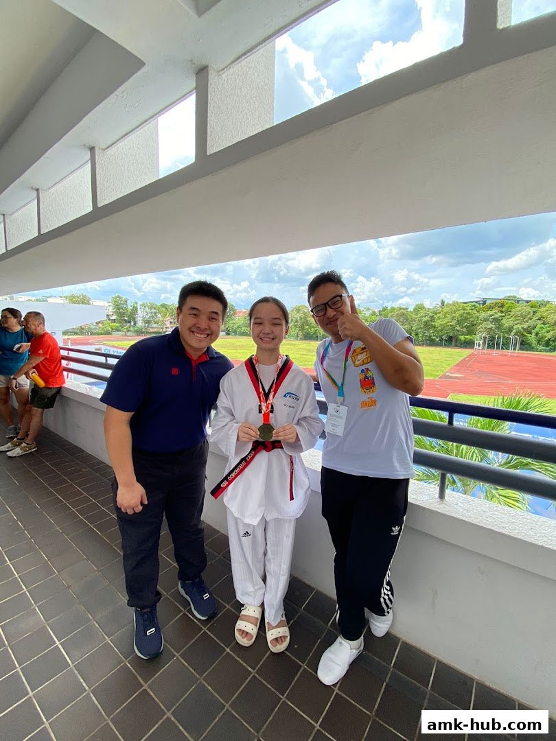 Three people, including a young Taekwondo athlete with a medal, pose for a photo.