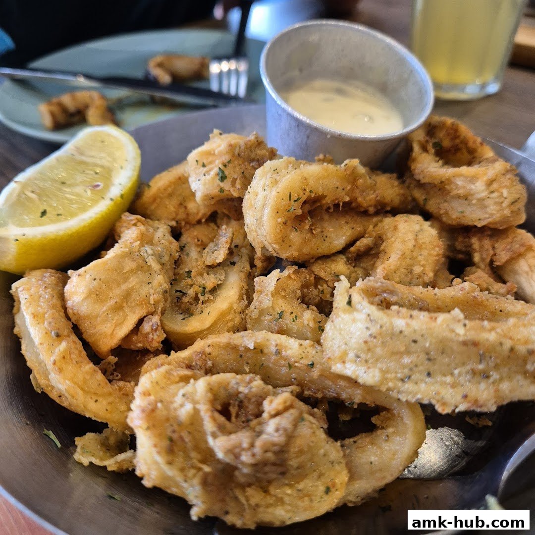 A close-up shot of crispy fried calamari served with a lemon wedge and dipping sauce.