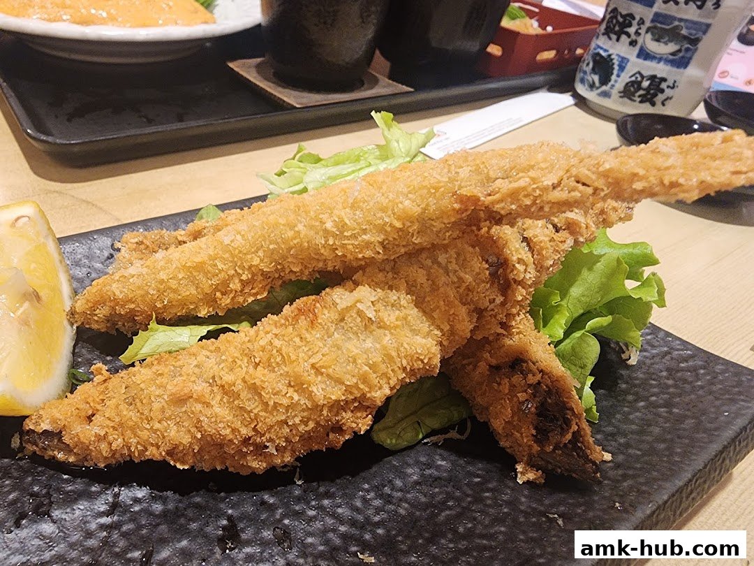 Crispy fried fish served with a lemon wedge and lettuce on a black plate.