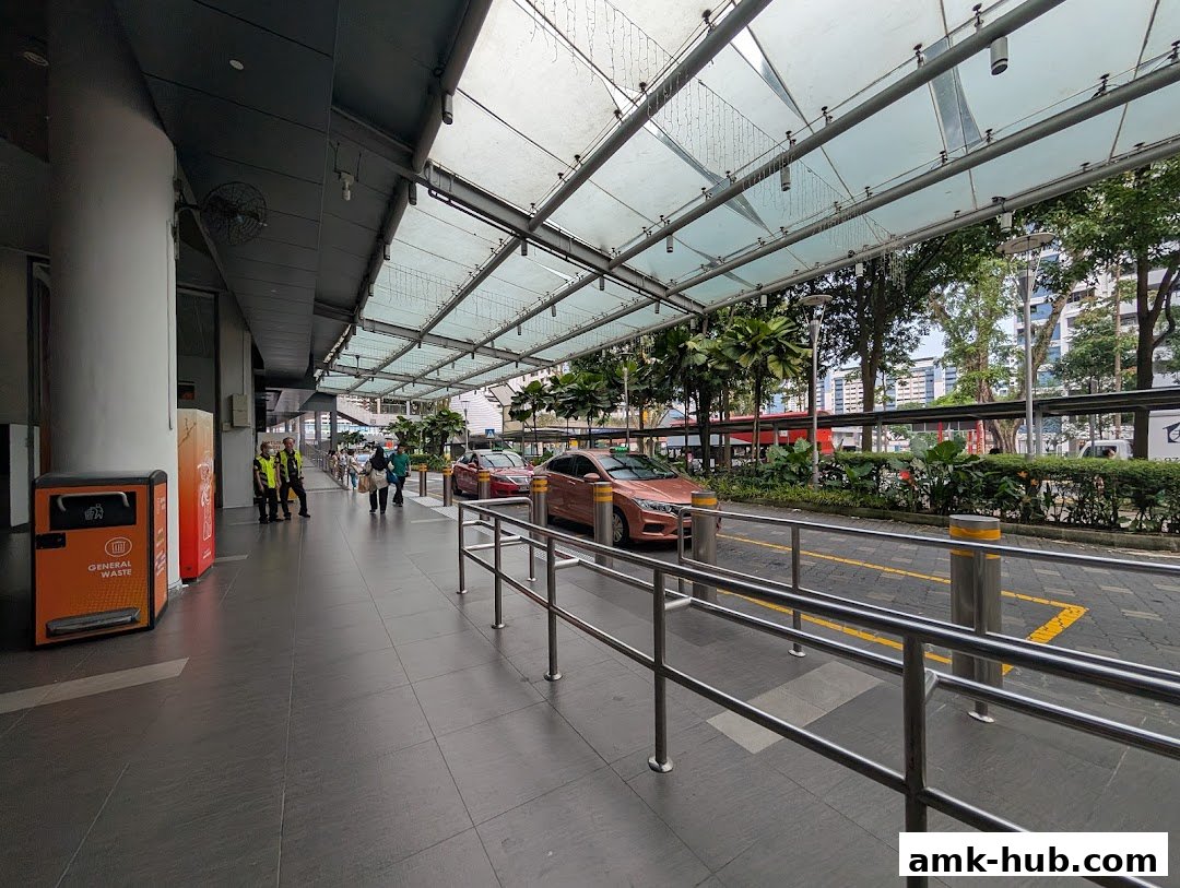 A covered walkway with taxis and people at a taxi stand outside a building.