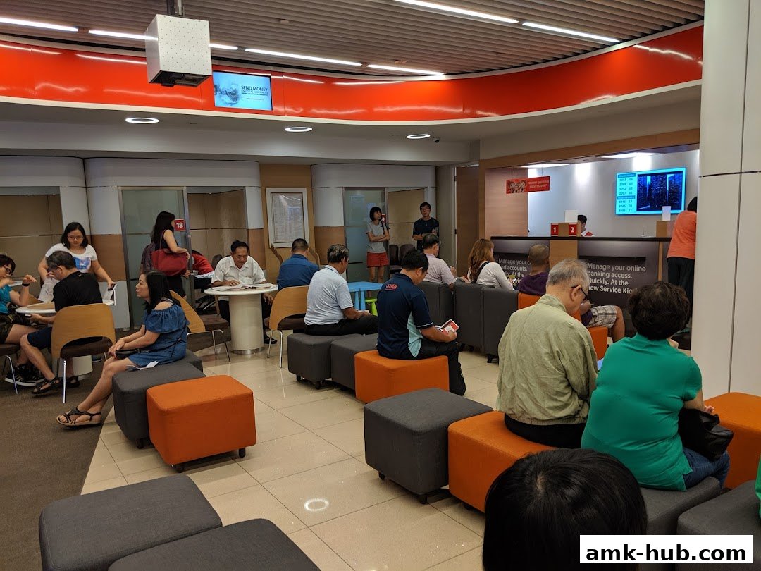 People waiting inside a bank branch with seating and service counters.