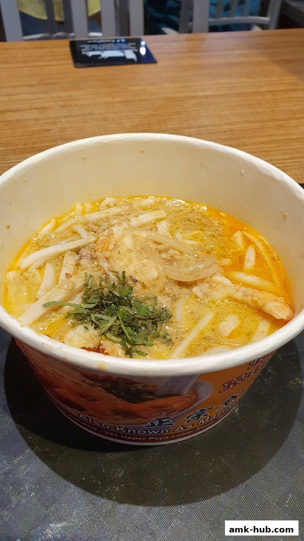 A close-up shot of a bowl of Laksa with noodles, broth, and garnishes.
