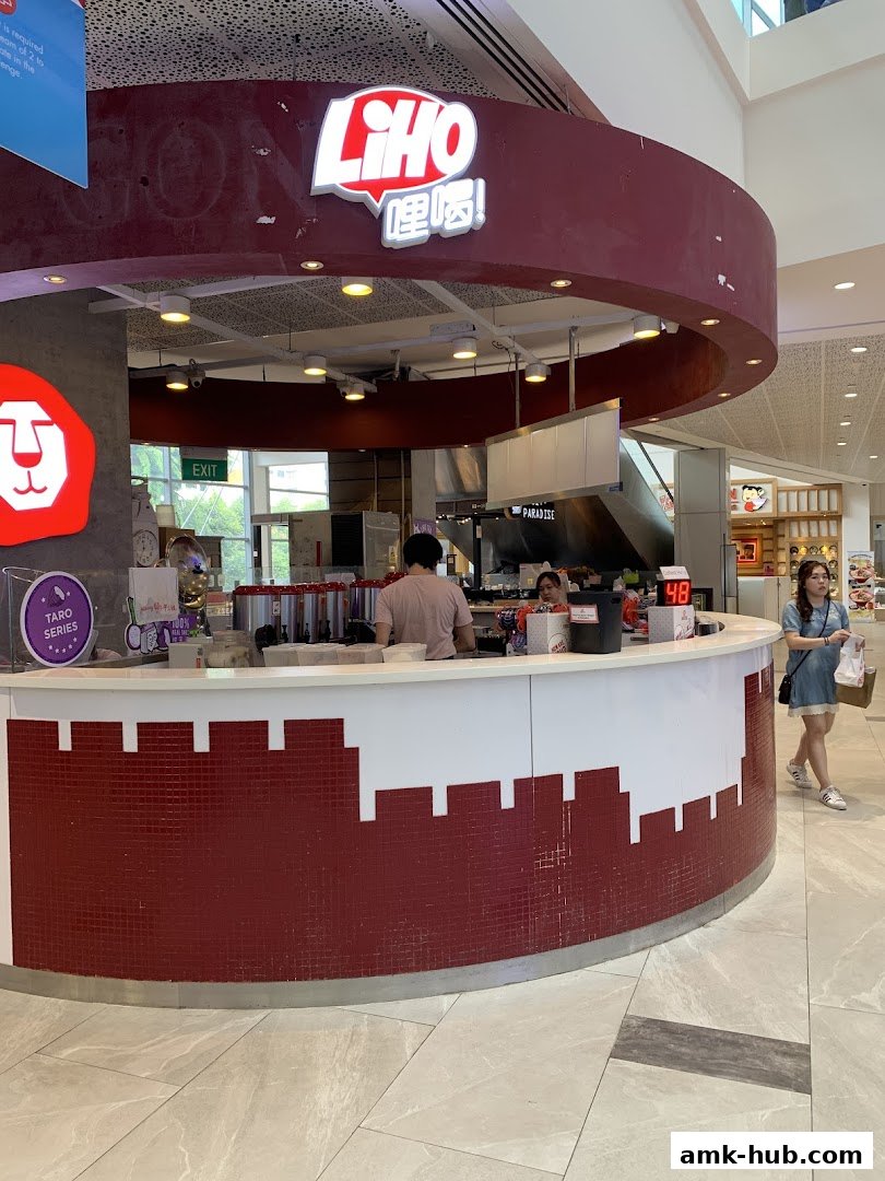 A LiHO TEA kiosk with staff serving customers and a woman walking by.