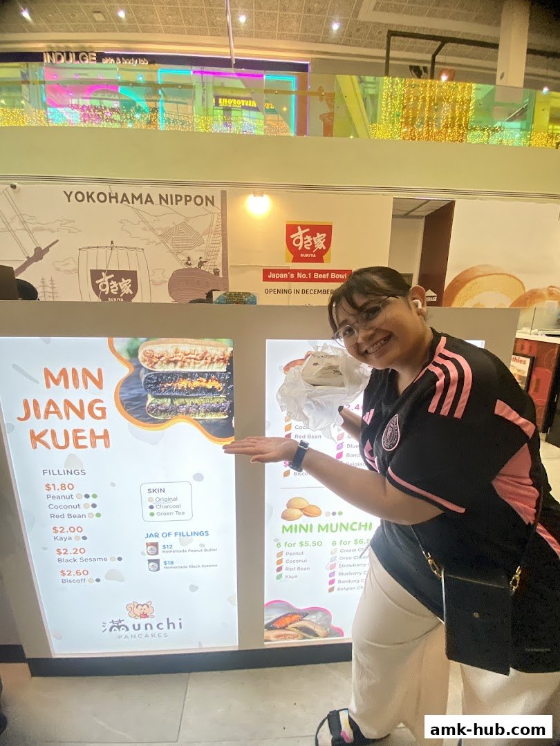 A woman poses in front of a brightly lit menu board for Munchi Pancakes.