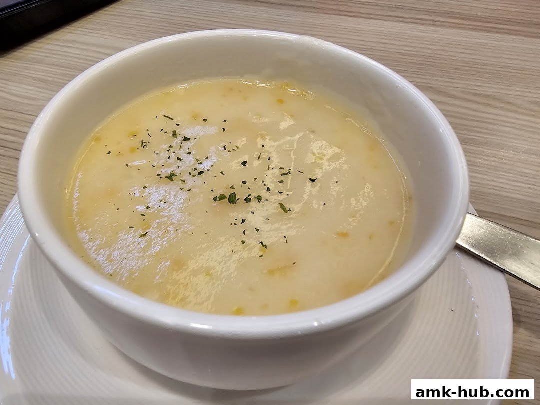 A close-up shot of a creamy corn soup in a white bowl, garnished with herbs.