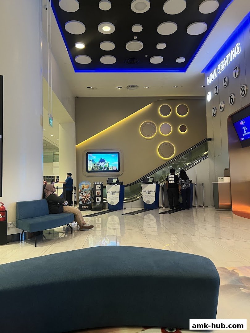 Interior of a modern cinema lobby with seating, ticket kiosks, and escalators.