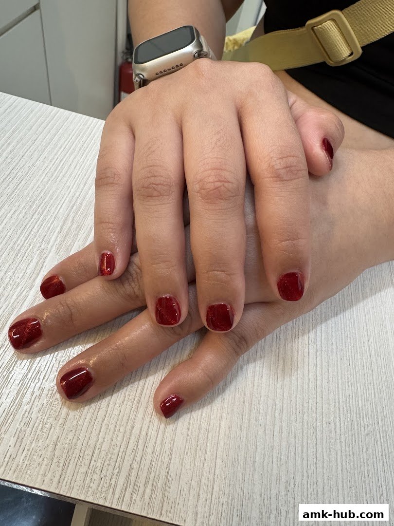 Close-up of hands with freshly painted dark red glitter gel nails.