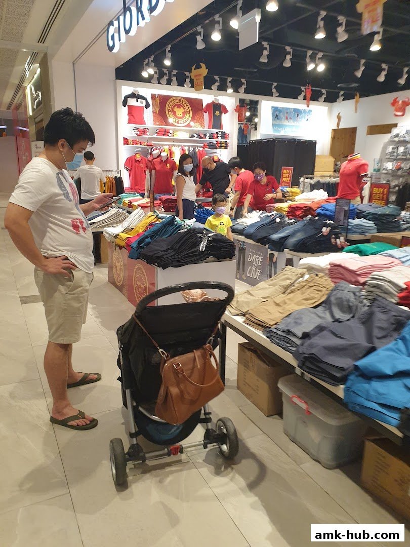 People shopping for casual wear at Giordano, with folded clothes and displays of t-shirts and pants.