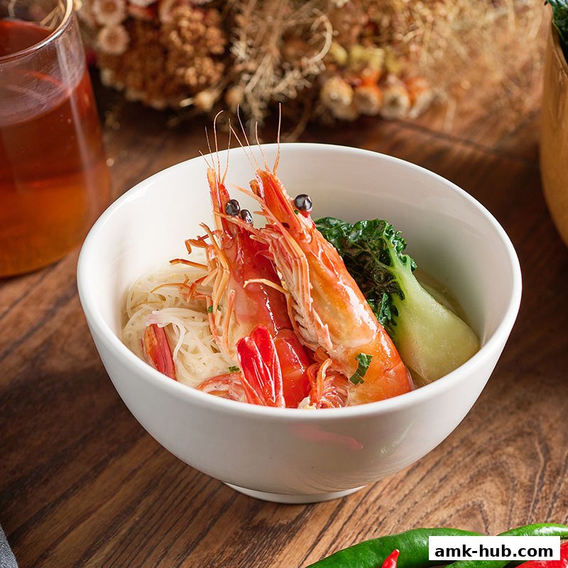 A bowl of prawn noodle soup with bok choy and a glass of iced tea.