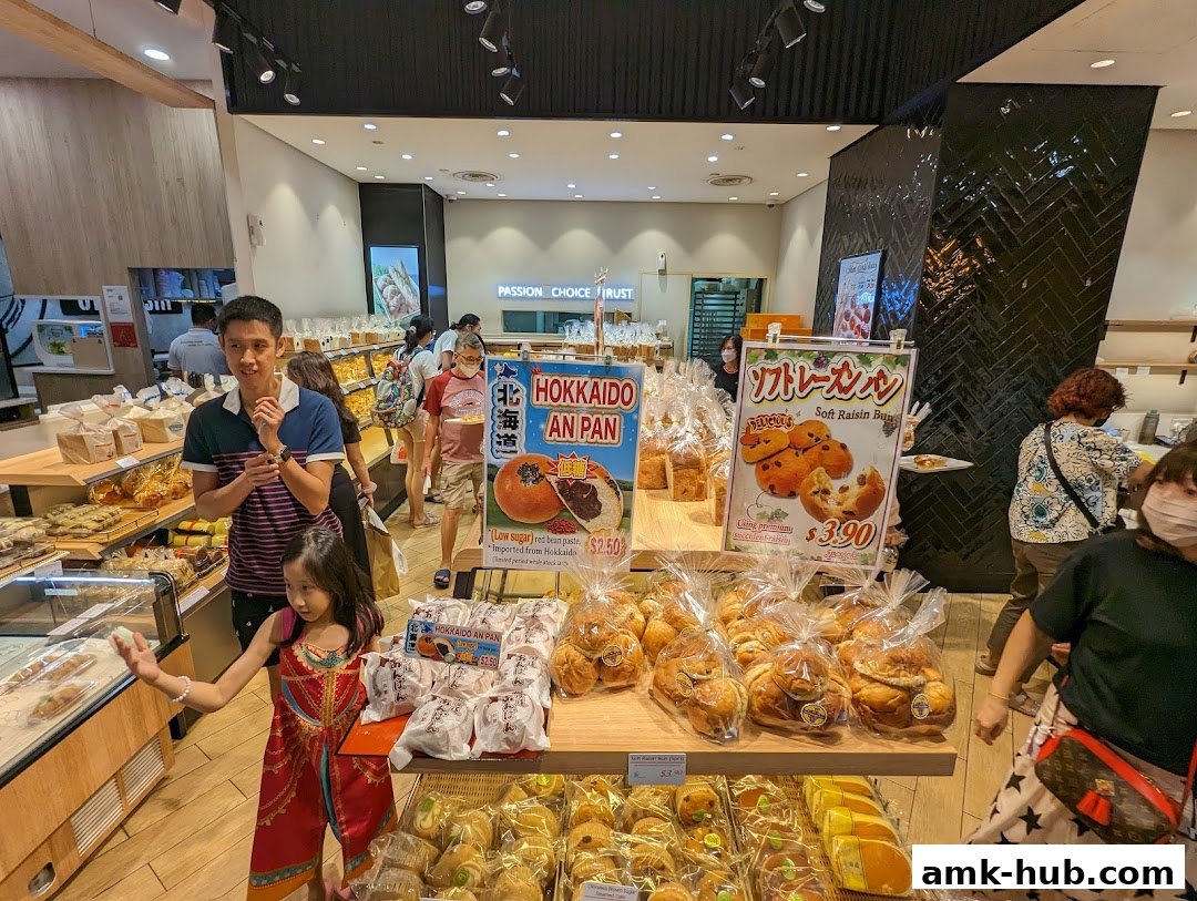 A bakery interior with customers browsing a wide selection of fresh bread and pastries.