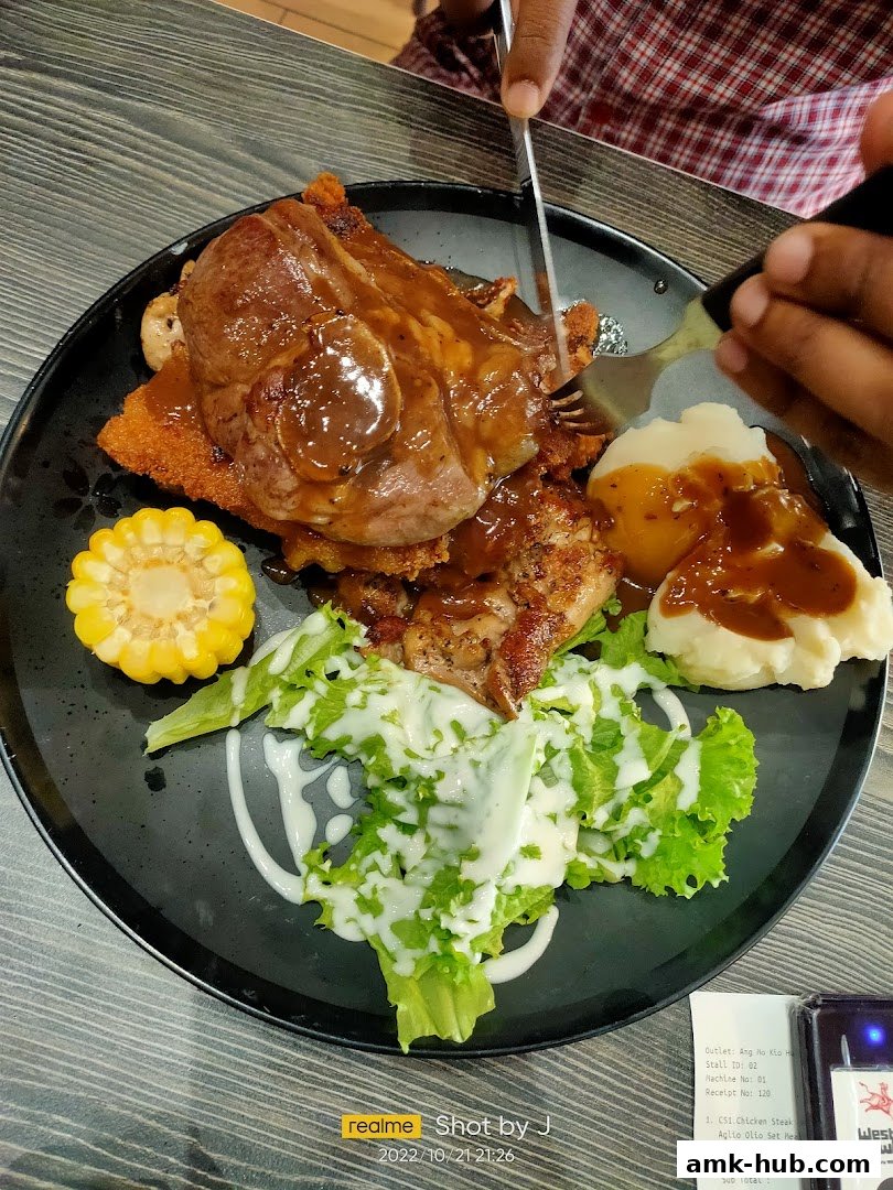 A person is cutting a steak with mashed potatoes, corn, and salad on a black plate.