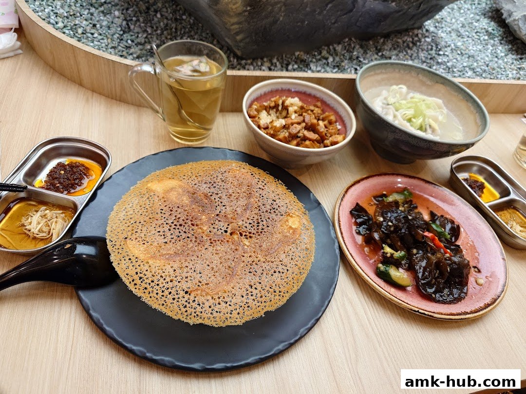 A table laden with various Chinese dishes, including dumplings, a crispy pancake, and side dishes with tea.