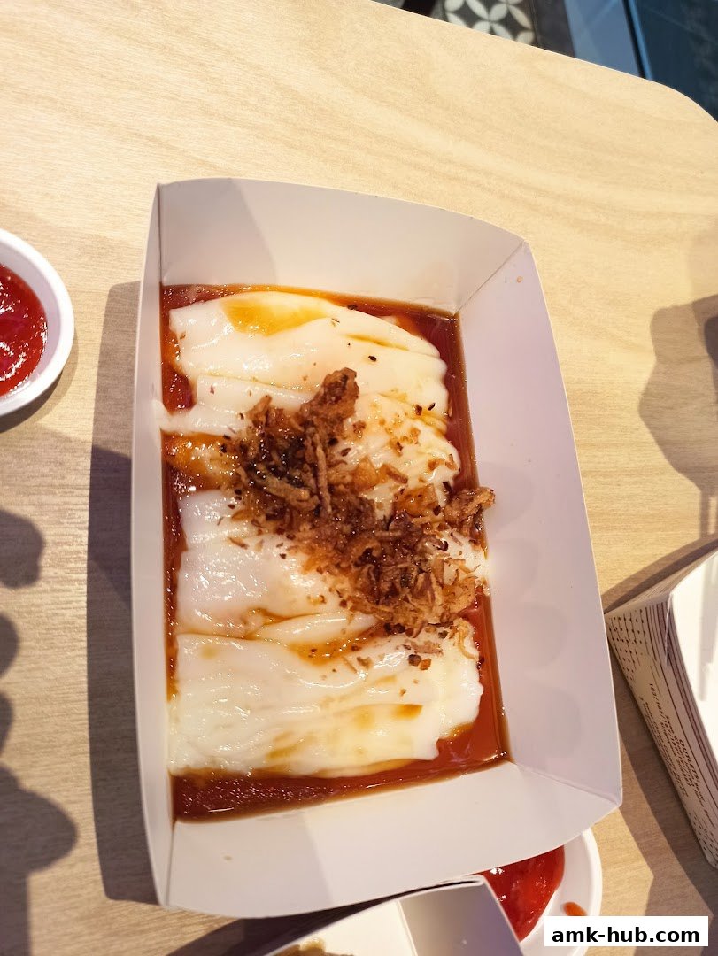 A close-up of a dish of chee cheong fun with sauce and crispy toppings.