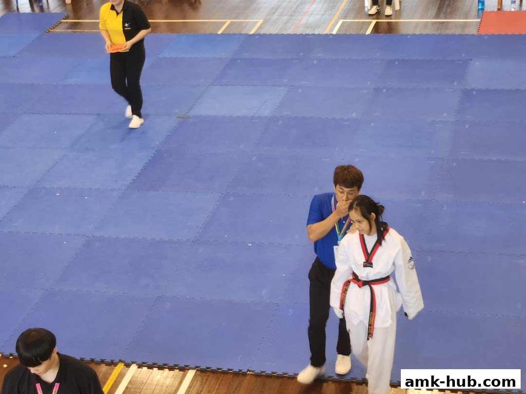 Taekwondo instructor guiding a student on a blue mat during a competition or training.
