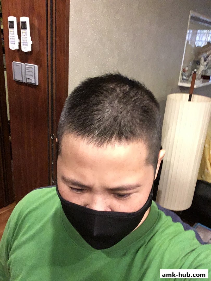 A person with a short haircut and a black face mask looks down.