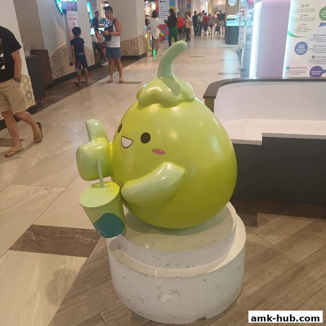 A cute green cartoon character holding a drink, posing in a shopping mall.
