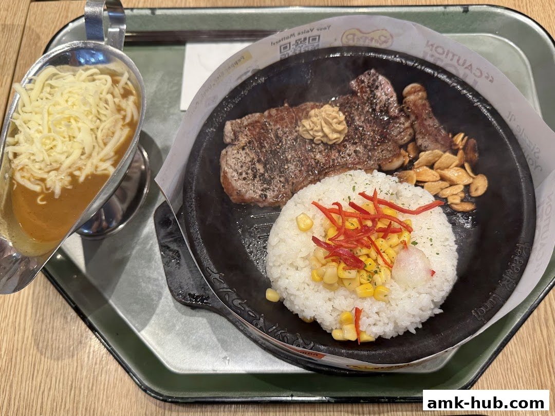 A sizzling steak served with rice, corn, and a side of curry sauce with cheese.
