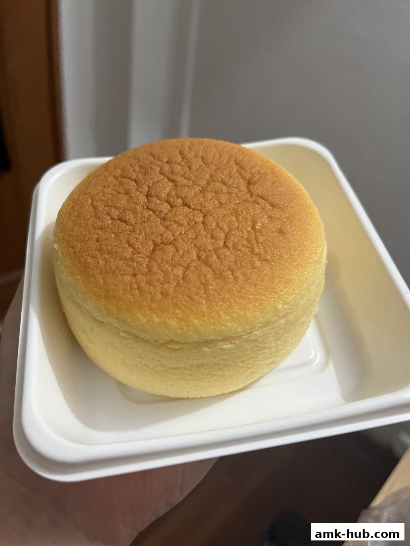 A close-up shot of a fluffy, golden-brown Japanese cheesecake in a white takeaway container.