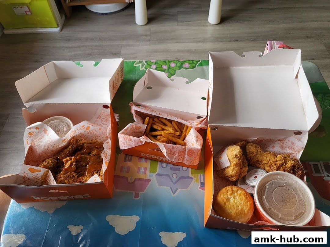 Three open Popeyes boxes filled with fried chicken, fries, a biscuit, and dipping sauce.