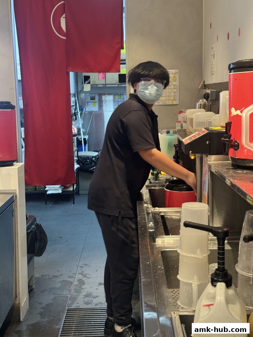A staff member in a mask and goggles prepares drinks behind the counter at LiHO TEA.