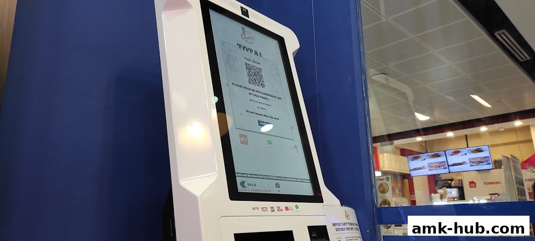 A self-service kiosk with a QR code for payment, next to a shop window displaying food.