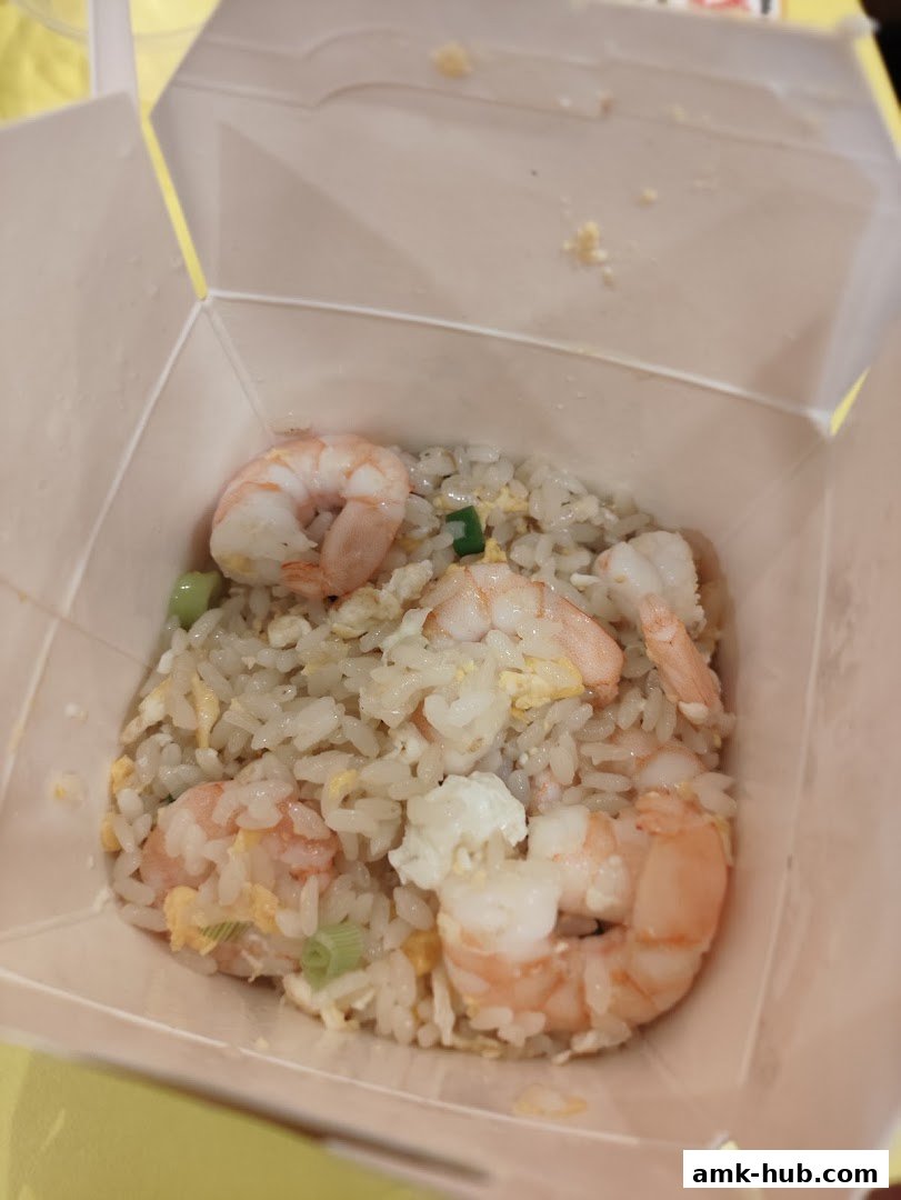 A close-up shot of a takeaway box filled with shrimp fried rice and green onions.