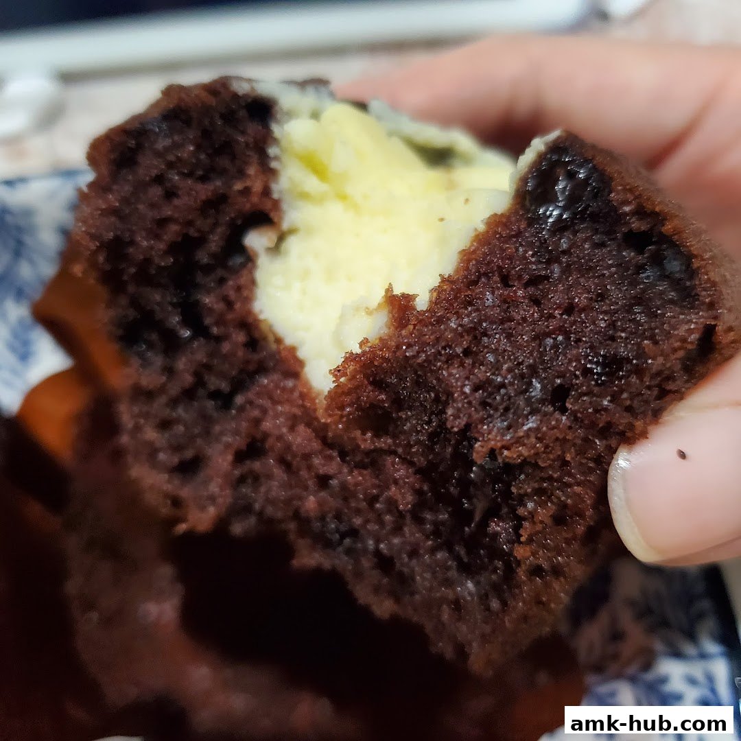A close-up shot of a chocolate muffin with a creamy filling being held.
