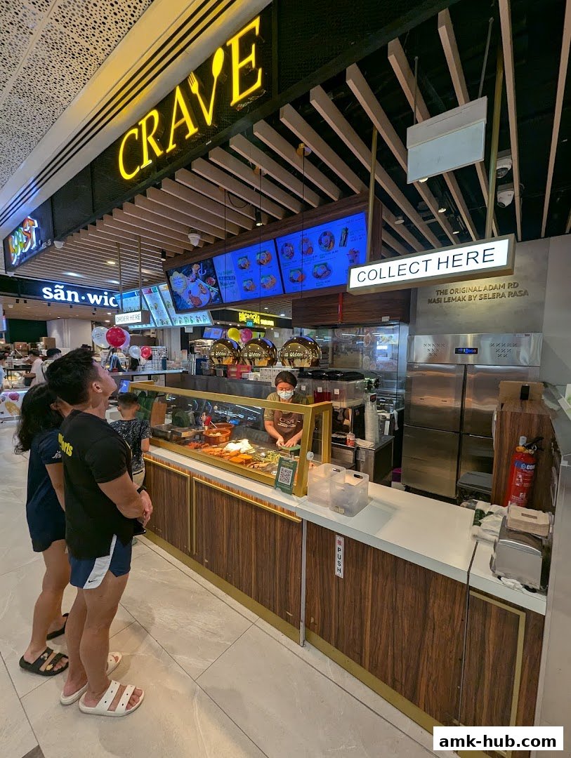 Customers queue at Crave Nasi Lemak, a food stall with a bright yellow sign and digital menu boards.