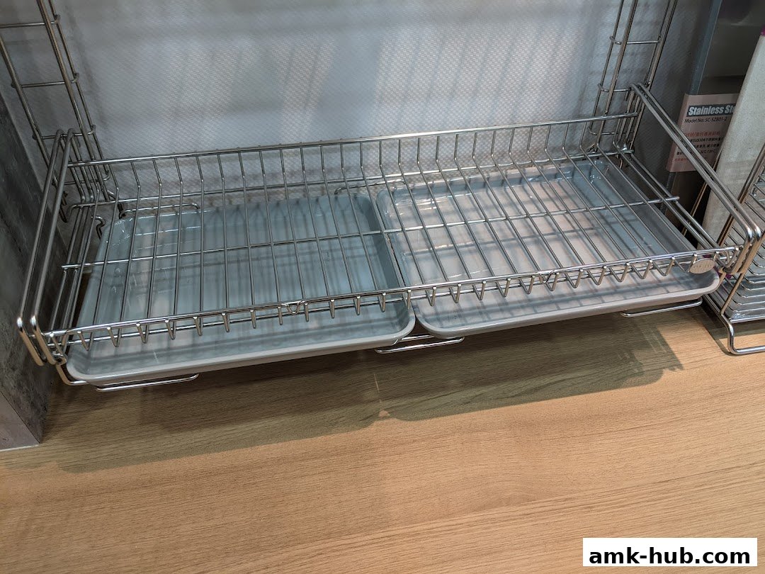 A stainless steel dish rack with two trays is displayed on a wooden surface.
