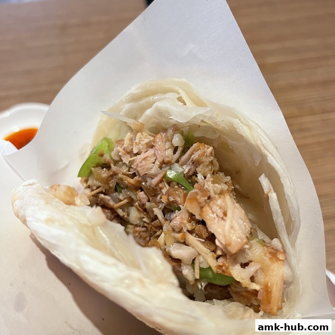 A close-up shot of a delicious shredded chicken wrap with a side of chili sauce.