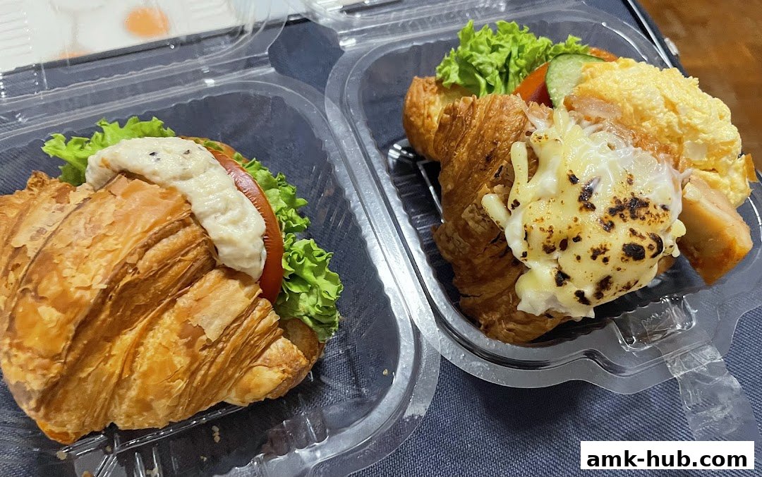 Two takeaway croissant sandwiches with fresh ingredients and melted cheese.