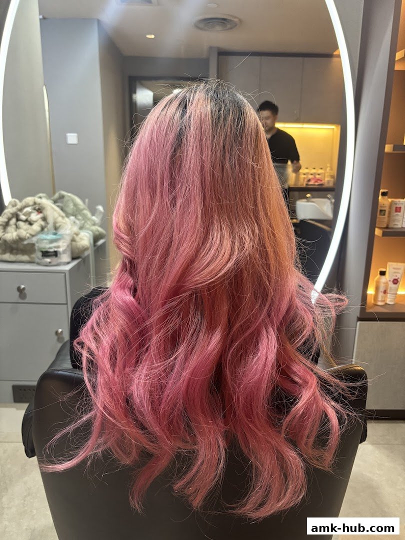 A person with vibrant pink, wavy hair sits in a salon chair, viewed from behind.