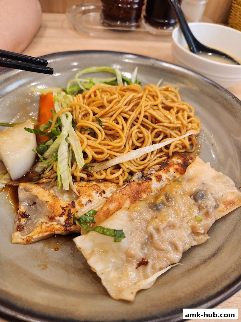 A close-up of a delicious meal featuring noodles, pan-fried dumplings, and a side of soup.