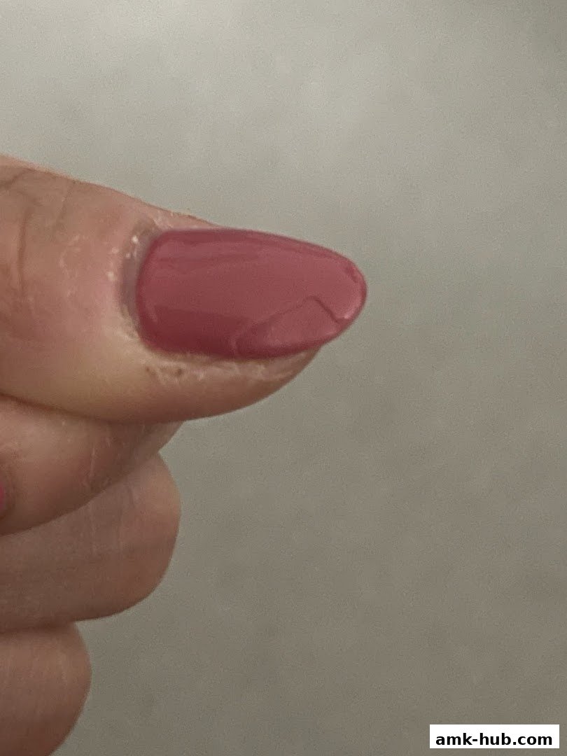 A close-up shot of a person's finger with a chipped, dusty rose colored nail polish.