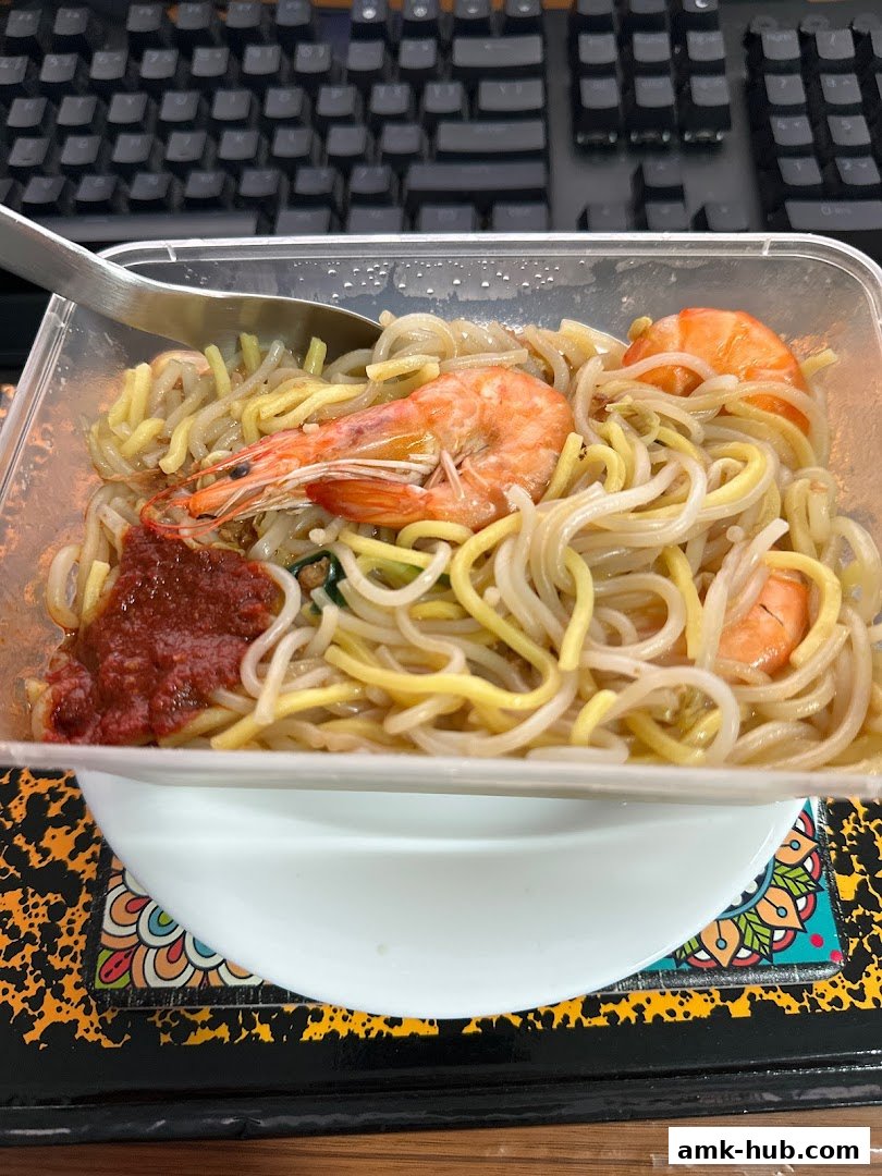 A close-up of Hokkien Mee with prawns and chili paste, served in a takeaway container.