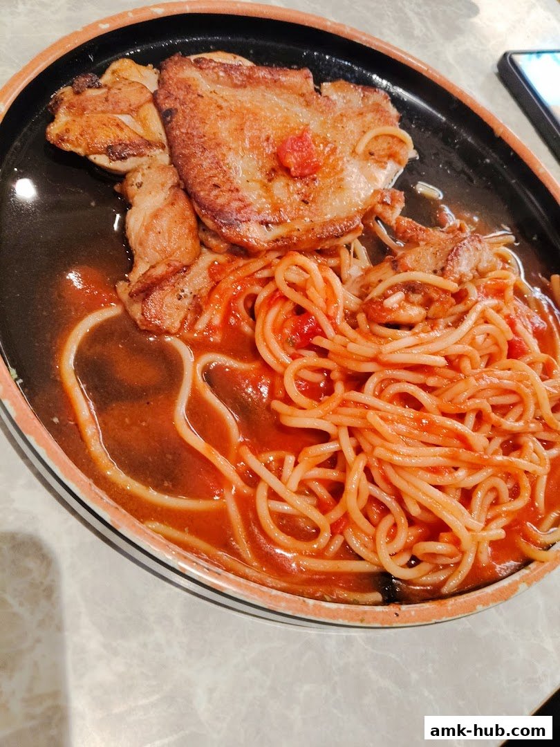A sizzling plate of spaghetti with chicken and tomato sauce, served in a black dish.