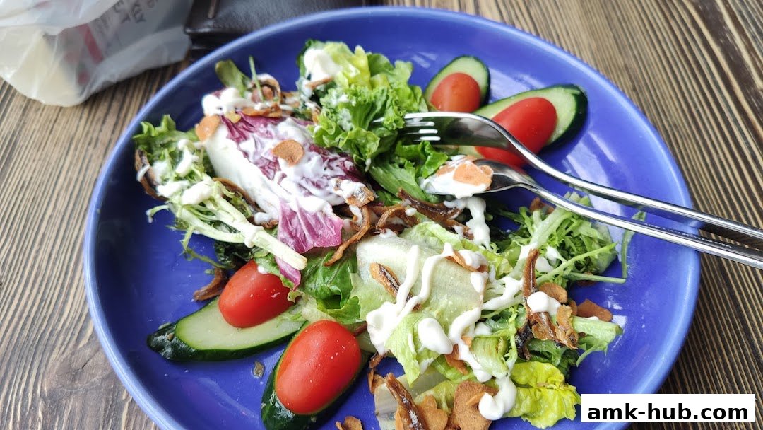 A vibrant salad with fresh lettuce, tomatoes, cucumbers, and a creamy dressing, served on a blue plate.