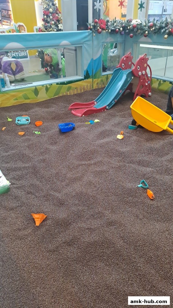 A children's indoor sandpit with a slide, toys, and a wheelbarrow.