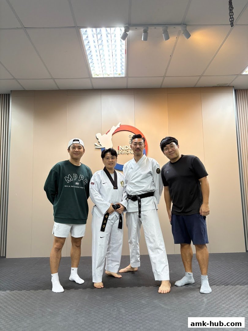 Four individuals, two in Taekwondo uniforms, pose in a training studio.