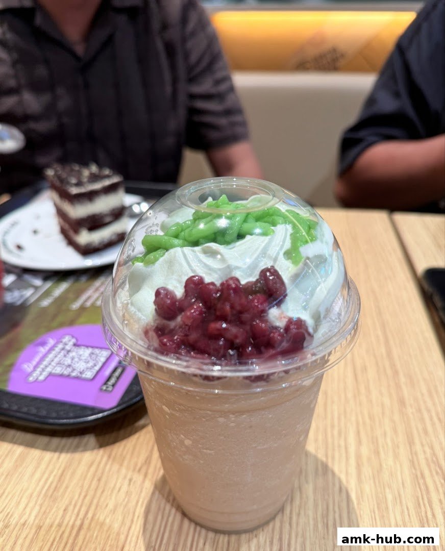 A close-up of a blended drink topped with whipped cream, red beans, and green jelly.